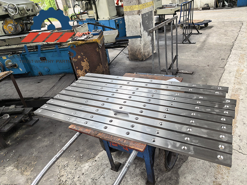 Un lote de hojas de corte de guillotina rectificadas con precisi&oacute;n y orificios de montaje avellanados apiladas en el taller de fabricaci&oacute;n de ALAS